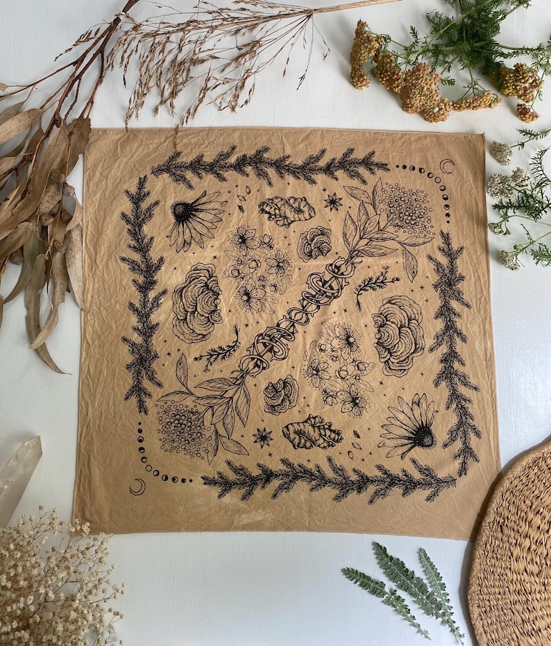 May include: A tan bandana with a black and white floral design. The design features flowers, leaves, and stars. The bandana is made of a soft, cotton fabric.