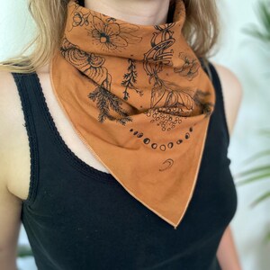 May include: A brown bandana with a black floral and moon phase design. The bandana is tied around a person's neck.