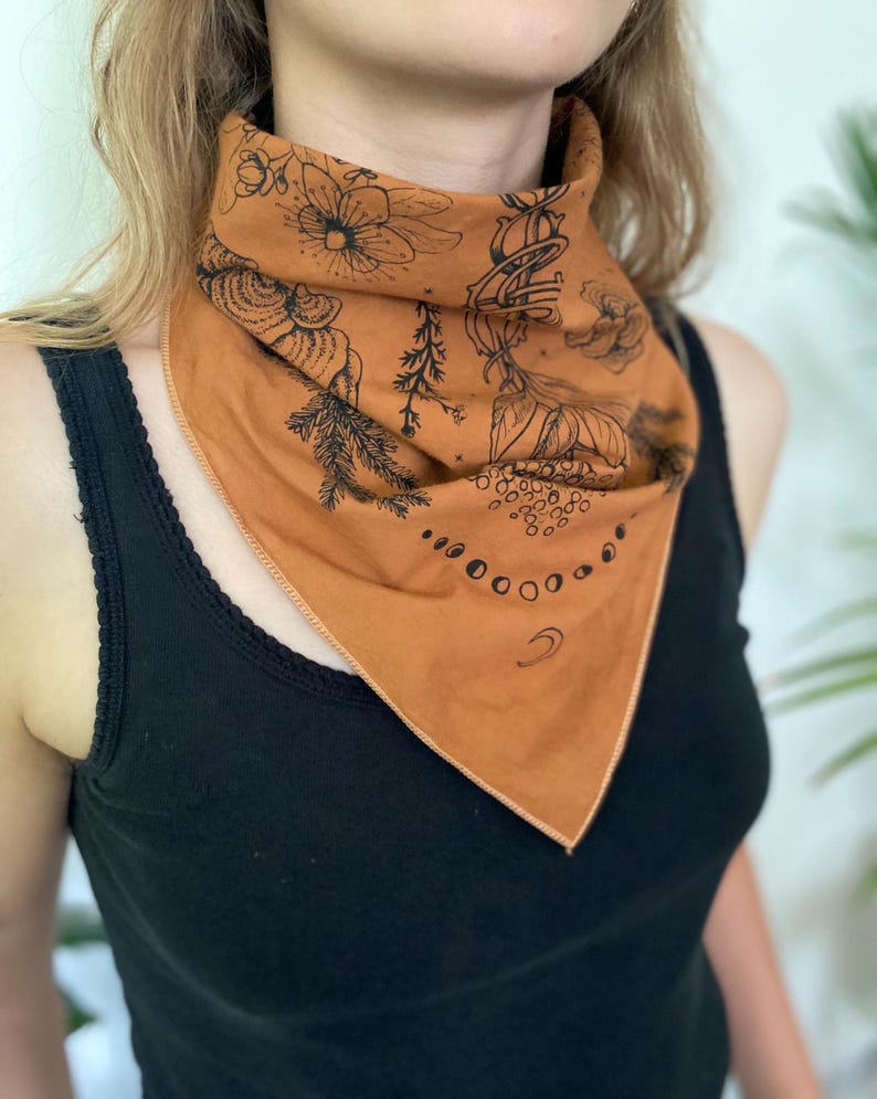 May include: A brown bandana with a black floral and moon phase design. The bandana is tied around a person's neck.