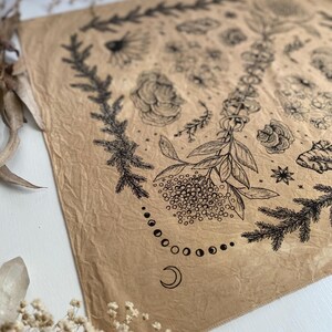 May include: A brown fabric bandana with a black and white floral design. The design includes flowers, leaves, and a crescent moon with a circle of smaller moons around it.