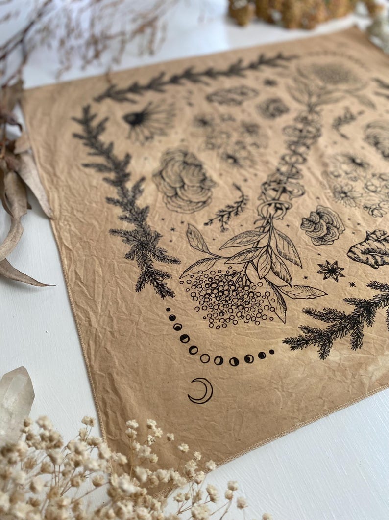 May include: A brown fabric bandana with a black and white floral design. The design includes flowers, leaves, and a crescent moon with a circle of smaller moons around it.