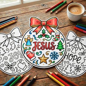 以下が含まれることがあります： 「喜び」と「希望」の文字が入ったクリスマスオーナメントの塗り絵と、「イエス」という文字が入った中央のオーナメント。中央のオーナメントは、赤いリボン、天使、星、その他のクリスマスのシンボルで着色されています。色鉛筆とコーヒーカップも写っています。