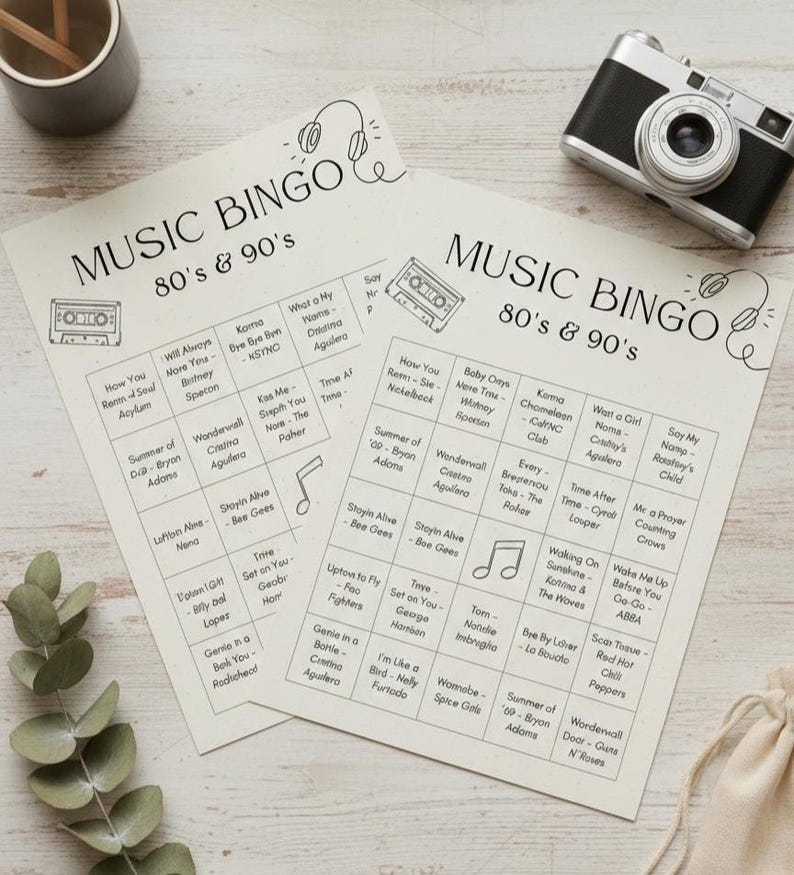 May include: Two Music Bingo cards with 80s & 90s music themes. The cards have a beige background with black text and illustrations of a cassette tape and headphones. A vintage camera and a small wooden pencil holder are also visible.