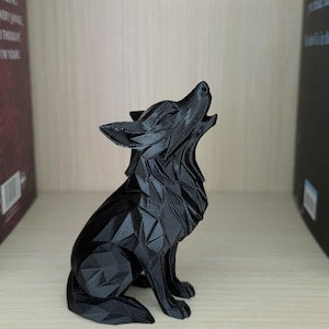May include: A black, geometric wolf ornament in a howling pose. The sculpture has a faceted design, giving it a modern look. It is made of a dark material and is displayed on a wooden shelf, showcasing its detailed craftsmanship.