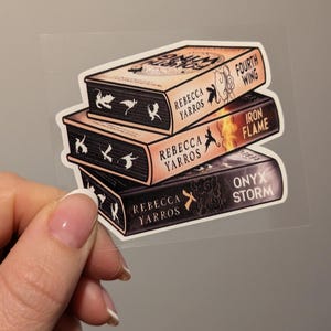 May include: A clear sticker depicting a stack of three books. The titles are "Fourth Wing", "Iron Flame", and "Onyx Storm". The books have a dark colour scheme with gold accents, and the author's name, Rebecca Yarros, is printed on each spine.
