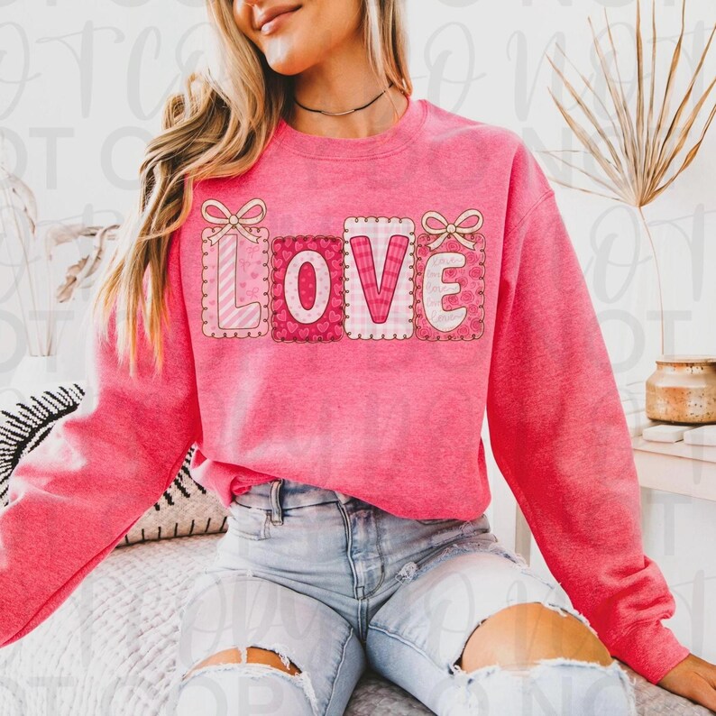 May include: A pink sweatshirt with the word "LOVE" in a patchwork design. The letters are in individual squares with different patterns, including stripes and hearts. Each square is outlined with a scalloped edge and topped with a bow.