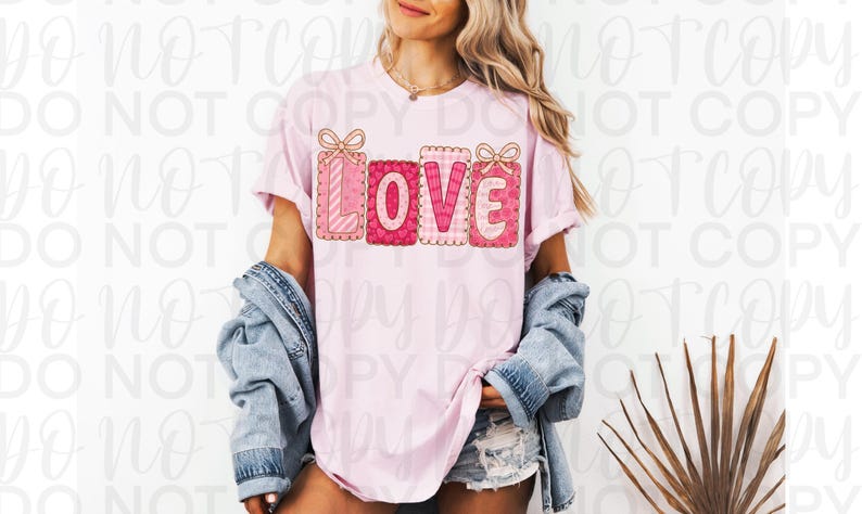 May include: A light pink t-shirt with the word "LOVE" in a decorative, gift-box style design. The letters are in shades of pink and red with bow accents. The shirt is worn with a denim jacket and shorts.