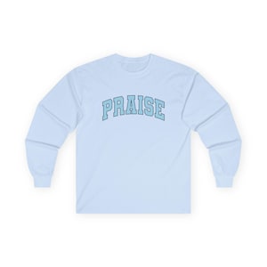 May include: A light blue long-sleeve shirt with the word "PRAISE" in light blue block letters across the chest. The word is outlined in a darker blue. The shirt has a crew neck and long sleeves.