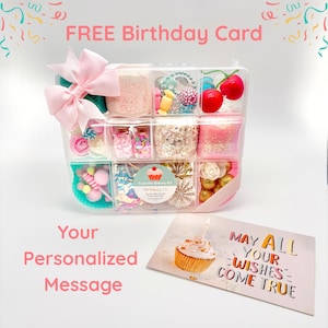 May include: A clear plastic organizer box filled with colorful craft supplies, including pink glitter, small glass jars, faux cherries, and decorative beads, topped with a large pink bow. A rectangular card features a cupcake and the text MAY ALL YOUR WISHES COME TRUE.