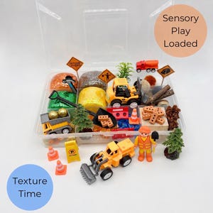 May include: A clear plastic container filled with construction-themed sensory play items. Includes toy trucks, cones, signs, play dough, and a construction worker figurine. The text "Sensory Play Loaded" and "Texture Time" are visible.