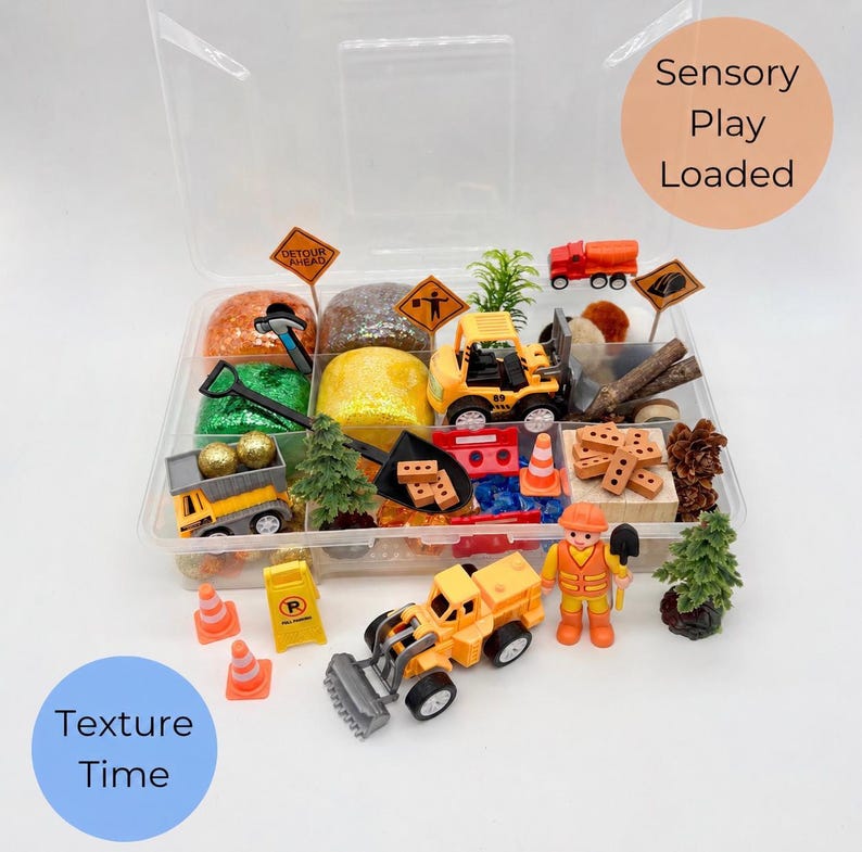 May include: A clear plastic container filled with construction-themed sensory play items. Includes toy trucks, cones, signs, play dough, and a construction worker figurine. The text "Sensory Play Loaded" and "Texture Time" are visible.