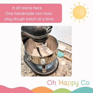 May include: A dark gray stand mixer with a stainless steel bowl containing a white flat beater attachment. The text reads: It all starts here. One handmade non-toxic play dough batch at a time. The brand name Oh Happy Co is visible at the bottom.