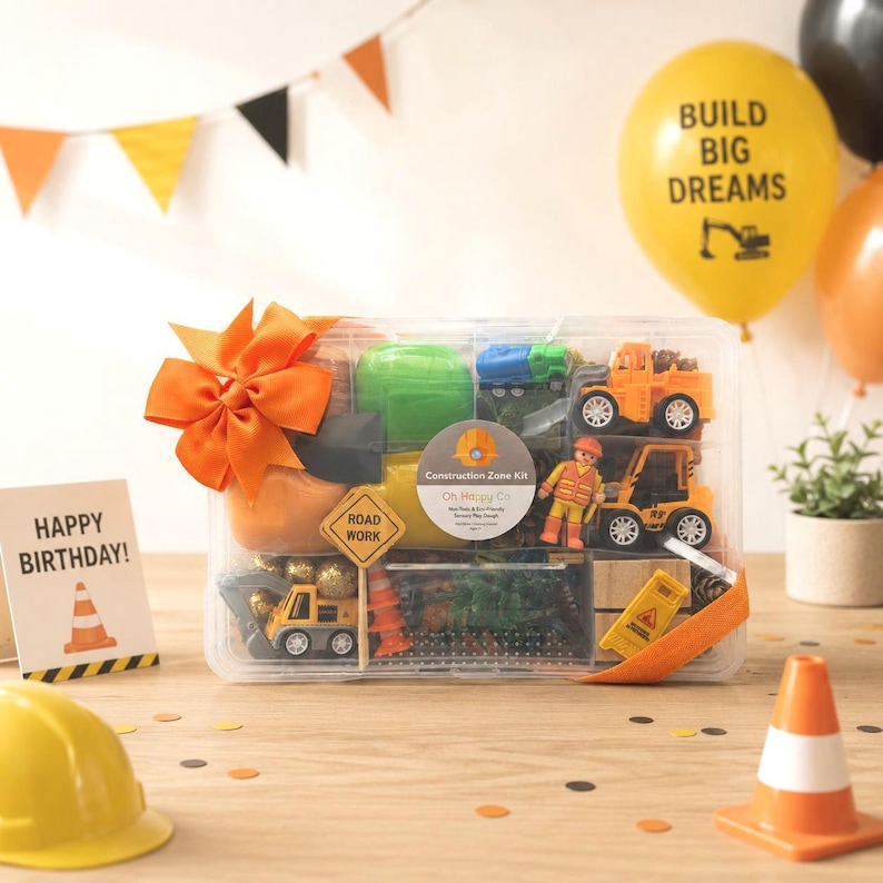 May include: A Construction Zone Kit with toy trucks, construction signs, and play dough, perfect for a birthday. The kit includes a card that says "Happy Birthday!" and a yellow balloon that says "Build Big Dreams".