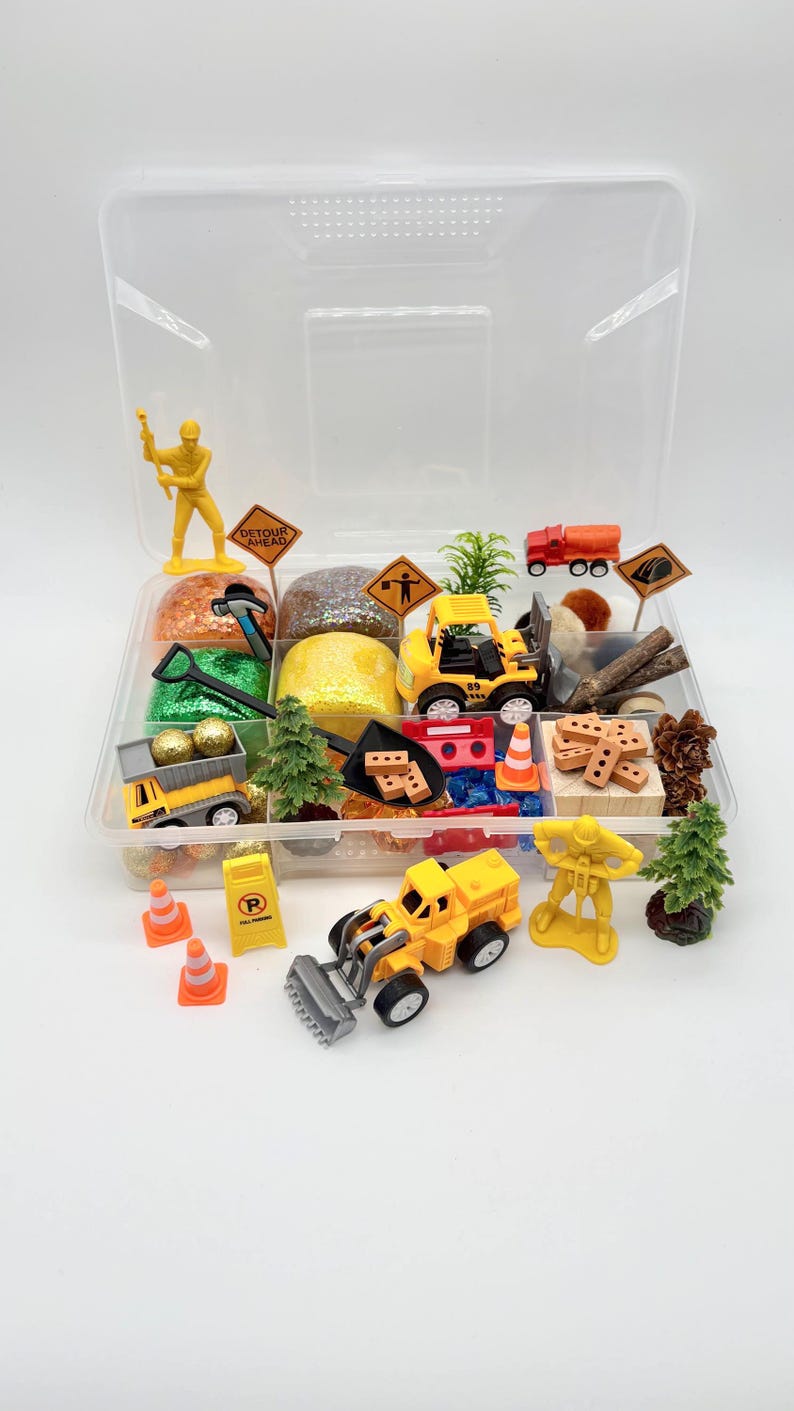 May include: A clear plastic container filled with miniature construction-themed toys and accessories. Includes yellow construction vehicles, traffic cones, signs, trees, and glittery play dough. The set is designed for imaginative play and creative exploration.