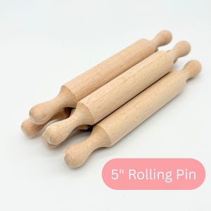 May include: A white ceramic mug with a black handle and the text "But First, Coffee" in a black, handwritten-style font. The mug is on a white surface.