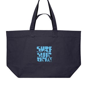 May include: A dark navy blue tote bag with two shoulder straps and a rectangular base. Centered on the front is a light blue graphic print featuring the text SURF SLEEP REPEAT in a stylized, blocky font that fills the central area of the bag.