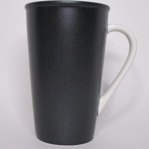 May include: A tall, black ceramic mug with a white handle. The mug has a textured surface and a simple, elegant design. The mug is suitable for hot or cold beverages.