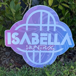 May include: A sign featuring the name "ISABELLA" in white, with "HUNTRAX" beneath, set against a purple and blue gradient. The sign is cloud-shaped with white decorative lines and star accents.