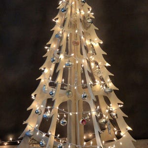 May include: A wooden Christmas tree with a unique open design. The tree is decorated with silver ornaments and white string lights. The tree is approximately 5 feet tall.