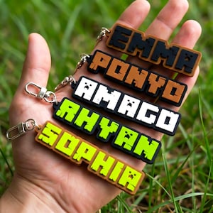 May include: Five personalized name keychains in various colors, including black, brown, white, and green. Each keychain features a different name in a pixelated font, with a silver clasp for attachment.