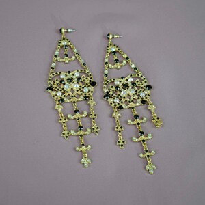 May include: A pair of gold-tone dangle earrings with black and clear rhinestones. The earrings feature a delicate, intricate design with multiple layers of chains and beads.