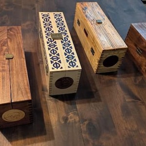 Peut inclure: Quatre boîtes rectangulaires en bois avec couvercles à charnières et loquets métalliques. Une boîte est en bois brun foncé, une en bois clair avec des motifs géométriques bleus, une en bois clair avec des gravures linéaires et une en brun foncé avec des incrustations circulaires vertes et orange.