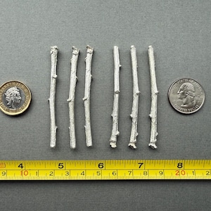 Könnte beinhalten: Sechs silberfarbene, zweigförmige Objekte liegen auf einer grauen Oberfläche, neben einer britischen Münze und einem US-Vierteldollar. Ein gelbes Maßband zeigt, dass die Zweige etwa 7,6 bis 10,2 cm lang sind.