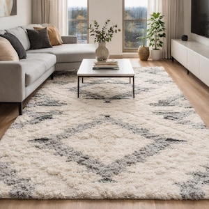 Peut inclure: Un grand tapis shaggy avec un motif géométrique en blanc, gris et noir. Le tapis est placé dans un salon avec un canapé gris, une table basse et une télévision. Idéal pour un espace de vie.