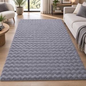 Peut inclure: Un tapis rectangulaire de couleur gris clair uni présentant une texture ondulée ou ridée répétitive et cohérente sur toute sa surface. Le tapis a un aspect doux et moelleux et est posé à plat sur un sol en bois de couleur claire.