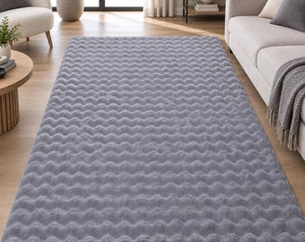 May include: A rectangular area rug in a solid light gray color featuring a consistent, repeating wavy or rippled texture across its entire surface. The rug has a soft, plush appearance and is laid flat on a light-colored wooden floor surface.