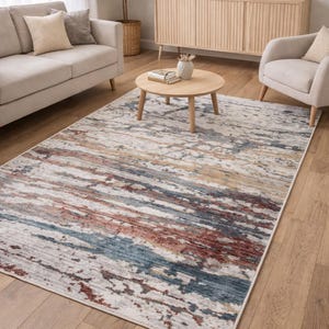 May include: A rectangular area rug with a distressed, abstract design. The rug features a blend of colors, including white, blue, red, and tan, creating a textured, painterly effect. It is placed on a hardwood floor in a living room setting.