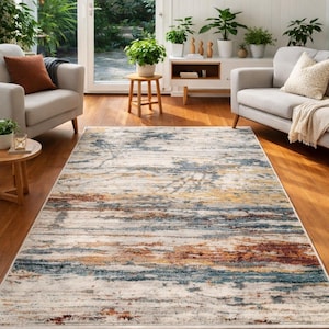 May include: A rectangular area rug with a distressed, abstract design. The rug features a blend of colors including cream, blue, gold, and rust. It is placed on a hardwood floor in a living room setting, with neutral-toned furniture and plants.