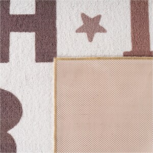 May include: A close-up of a white and brown rug with large letters and a star design. The rug has a textured surface and a tan border. The back of the rug is a light pink color.