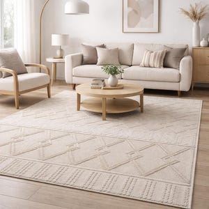 Könnte beinhalten: Ein neutrales Wohnzimmer mit beigem Sofa, Kissen und einem runden Couchtisch aus Holz. Ein gemusterter Teppich mit geometrischem Design bedeckt den Boden. Der Raum ist mit einer Stehlampe und Kunstwerken dekoriert. Teppichmaße in cm.