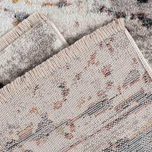 May include: Close-up of a beige area rug with a distressed pattern. The rug features a mix of colors, including gray, brown, and yellow, creating a vintage look. The edges have a fringed detail.