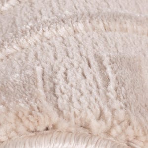May include: Close-up of a cream-colored, fluffy textile. The fabric has a soft, textured appearance with visible fibers and a plush, inviting feel. The neutral color suggests a cozy, warm aesthetic, suitable for home decor.