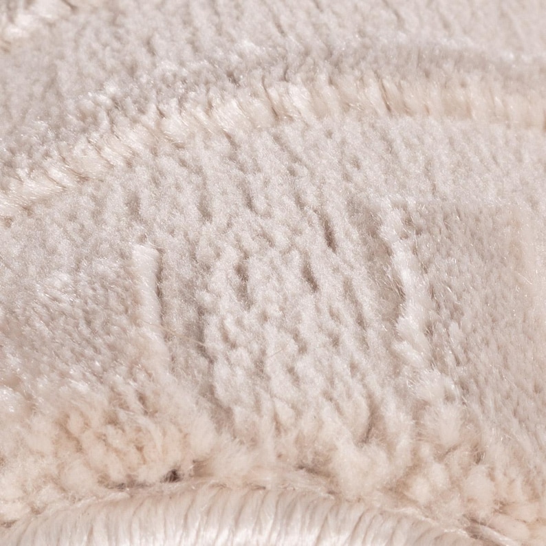 May include: Close-up of a cream-colored, fluffy textile. The fabric has a soft, textured appearance with visible fibers and a plush, inviting feel. The neutral color suggests a cozy, warm aesthetic, suitable for home decor.