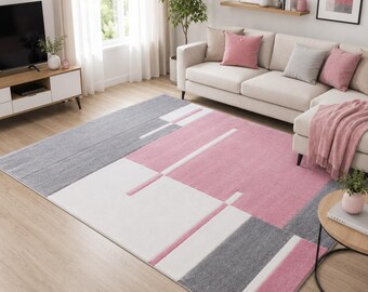 May include: A rectangular area rug featuring a geometric pattern with large blocks of soft pink, white, and light gray. The design consists of clean, straight lines and solid color sections that create a balanced, modern look across the floor surface.