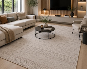 May include: A large rectangular area rug featuring a light beige color with a subtle, repeating geometric pattern of diamonds and horizontal bands. The rug is positioned in a living room setting, covering the floor space between a sofa and a chair.