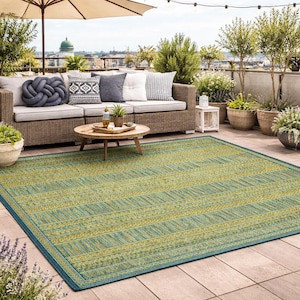 Könnte beinhalten: Ein rechteckiger Outdoor-Teppich mit einem gestreiften Muster in Grün und Gelb, umrandet von einem dunkelblauen Rand. Der Teppich liegt auf einer Terrasse mit einem Korbsessel, Kissen und einem runden Couchtisch aus Holz.
