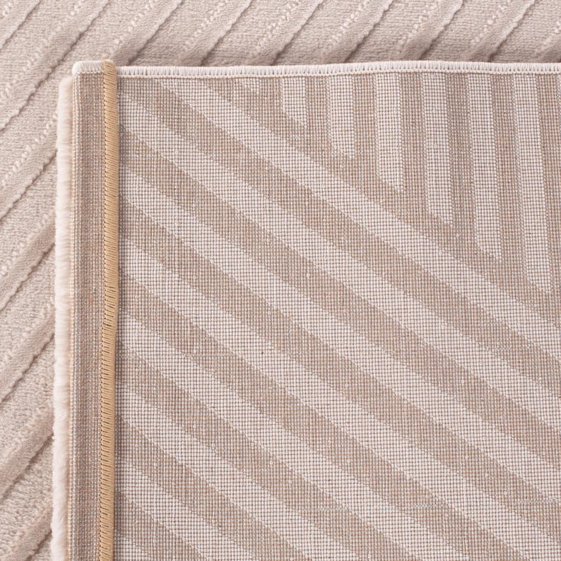 May include: Beige and tan area rug with a striped pattern. The rug has a textured surface and a contrasting border. The stripes run diagonally across the rug, creating a visual interest. The rug is made of a soft material.