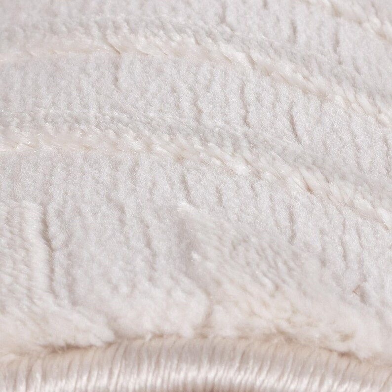 May include: Close-up of a soft, white, plush fabric with a textured surface. The material has a fluffy appearance with visible fibers and a subtle sheen, suggesting a cozy and comfortable texture.