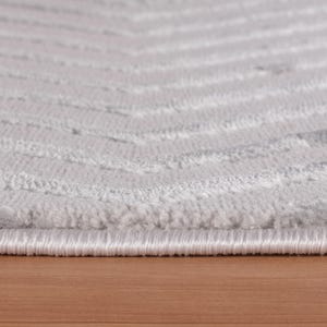 May include: Close-up of a light gray rug with a chevron pattern. The rug has a soft, textured surface with horizontal lines. The edges are finished with a white border. The rug is on a wooden surface.