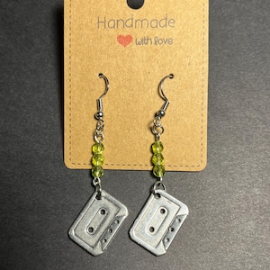 Könnte beinhalten: Handgefertigte Ohrringe mit silbernen Kassettenband-Anhängern und grünen Perlen. Die Ohrringe hängen an silbernen Haken und werden auf einer braunen Karte mit dem Text "Handmade with love" präsentiert.