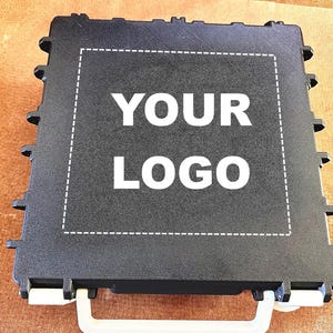 Puede incluir: Estuche rectangular negro con asa blanca y el texto "YOUR LOGO" en un rectángulo blanco. La funda tiene una superficie texturizada y pequeñas protuberancias en los bordes.