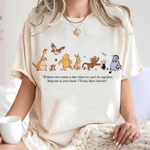 以下が含まれることがあります： クリーム色のTシャツ。カンガルー、クマ、ウサギ、トラなど、漫画のキャラクターのイラストが描かれています。シャツには「もし私たちが一緒にいられなくなる日が来ても、私のことを心に留めておいてください。私は永遠にそこにいます。」という引用があります。