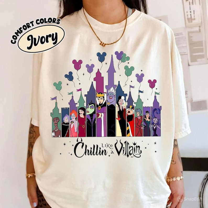 以下が含まれることがあります： アイボリー色のTシャツ。お城とディズニーヴィランズのグラフィックが特徴です。デザインには、ミッキーマウスの頭の形をした紫、緑、ピンクの風船が含まれています。Tシャツのテキストは「Chillin like a Villain」と書かれています。