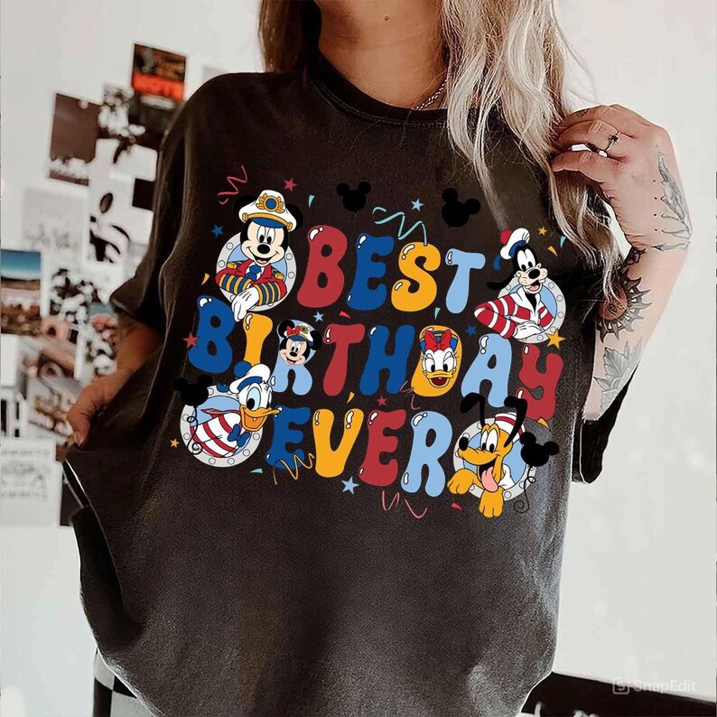 May include: Dark gray t-shirt featuring the phrase "BEST BIRTHDAY EVER" in colorful bubble letters, with cartoon characters Mickey Mouse, Minnie Mouse, Donald Duck, Goofy, and Pluto. The design includes stars and Mickey Mouse silhouettes.