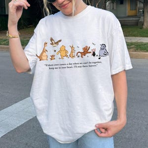 以下が含まれることがあります： カンガルー、クマ、トラなど、さまざまなキャラクターの漫画イラストが描かれたクリーム色のTシャツ。シャツには「もし私たちが一緒にいられなくなる日が来ても、私のことを心に留めておいてください。私は永遠にそこにいます」という引用句が表示されています。