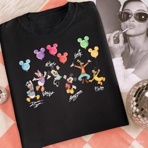 May include: Black crew neck sweatshirt featuring a colorful graphic of Disney characters holding balloon bouquets. The characters include Donald Duck, Daisy Duck, Minnie Mouse, Mickey Mouse, Goofy, and Pluto. The characters' names are written below them.
